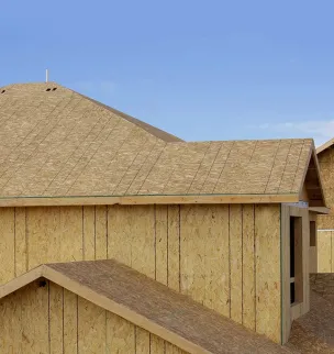 Newly constructed homes with exposed wood sheathing on roofs and walls under a clear blue sky.