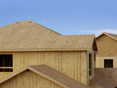 Newly constructed homes with exposed wood sheathing on roofs and walls under a clear blue sky.